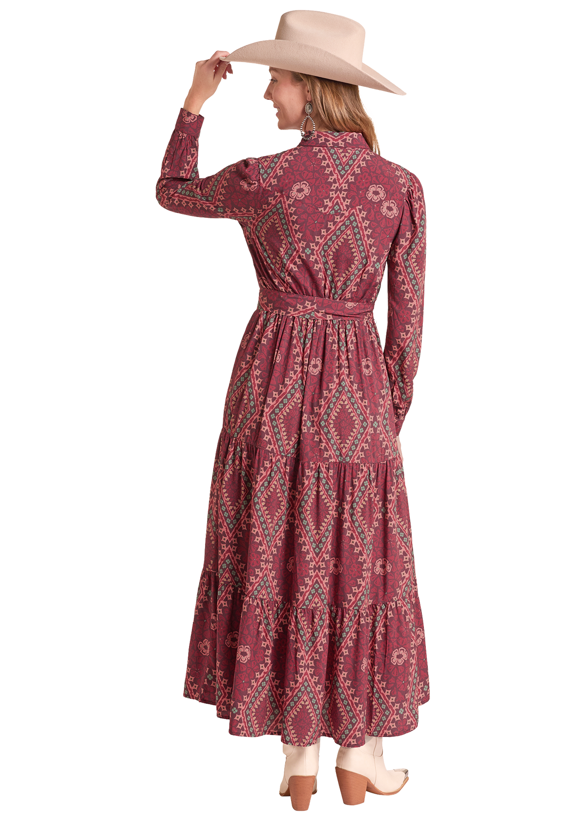 A woman wearing a long-sleeve, tiered maxi dress with a dusty rose and teal paisley pattern, paired with a beige wide-brim hat and white boots, shown from the back against a white background.