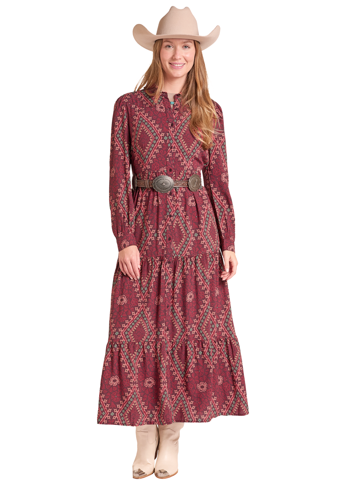 A woman modeling a long-sleeve midi dress with a rust red and teal geometric pattern, styled with a wide brown belt and a beige cowboy hat, on a solid white background.