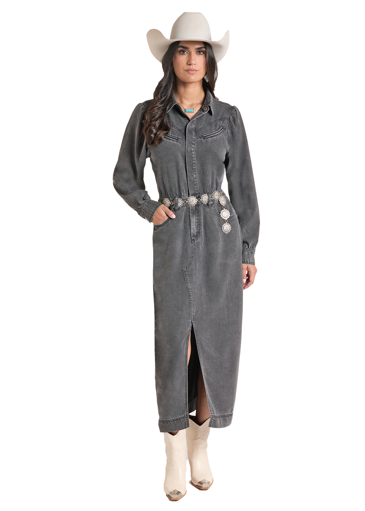 A woman modeling a long charcoal gray denim shirt dress with a western belt, silver conchos, and a cream cowboy hat, paired with cream boots, on a solid white background.