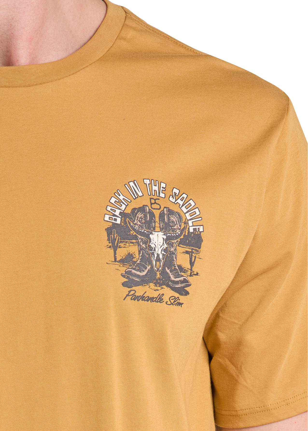 A close-up of a person wearing a mustard yellow t-shirt with a dark gray graphic on the left chest that reads 'BACK IN THE SADDLE IS Ponderosa Stn' around an illustration of a skull and saddle.