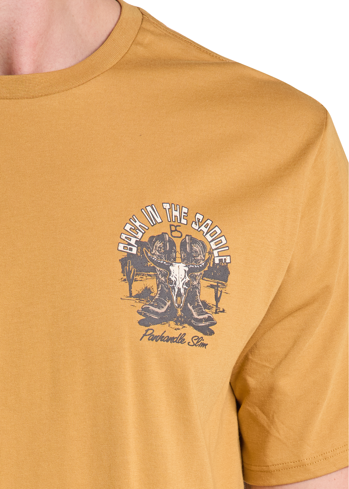 A close-up of a person wearing a mustard yellow t-shirt with a dark gray graphic on the left chest that reads 'BACK IN THE SADDLE IS Ponderosa Stn' around an illustration of a skull and saddle.