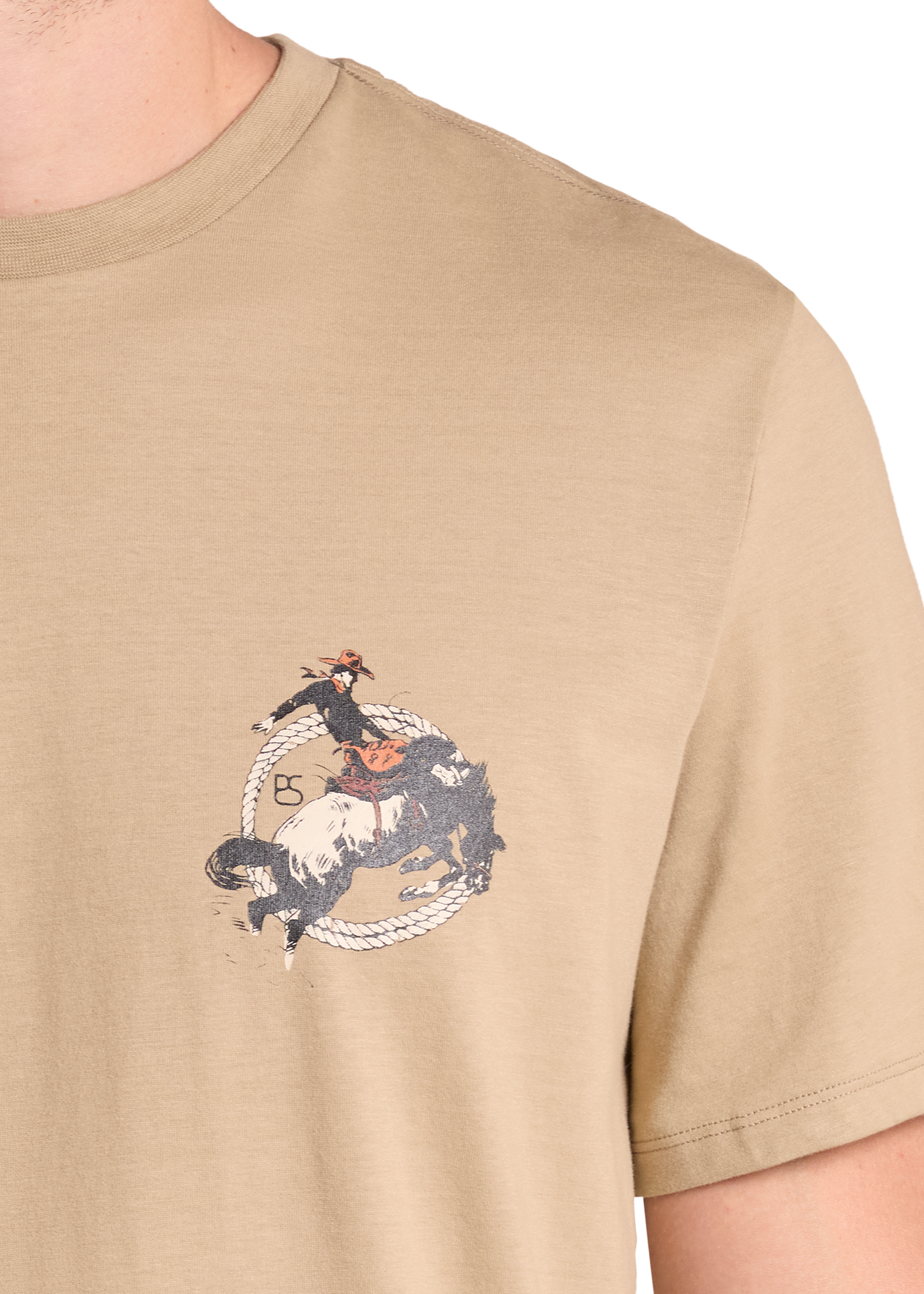 A close-up of a beige crewneck t-shirt featuring a graphic print of a cowboy riding a bucking horse in a lasso circle, worn by a model.