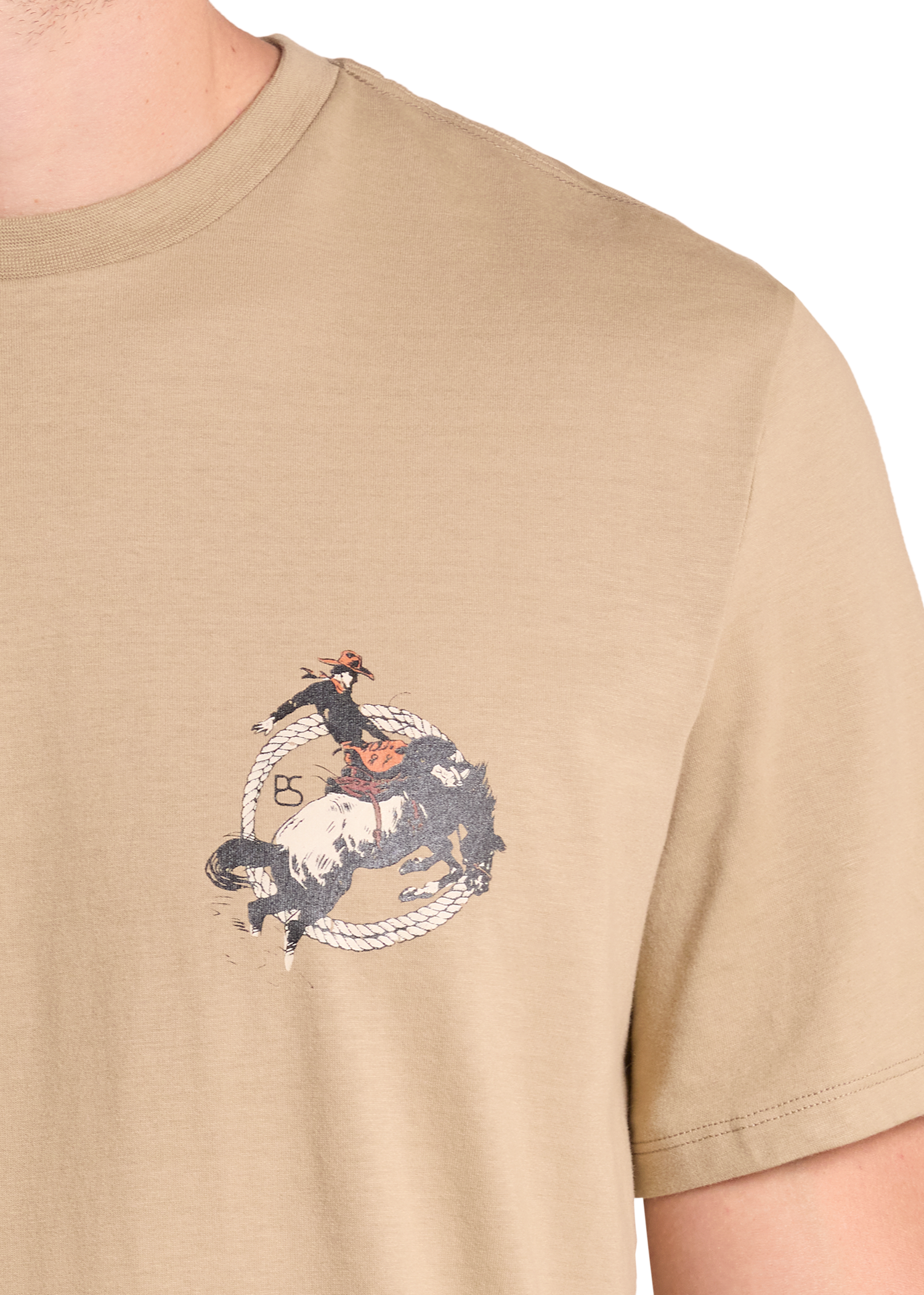 A close-up of a beige crewneck t-shirt featuring a graphic print of a cowboy riding a bucking horse in a lasso circle, worn by a model.