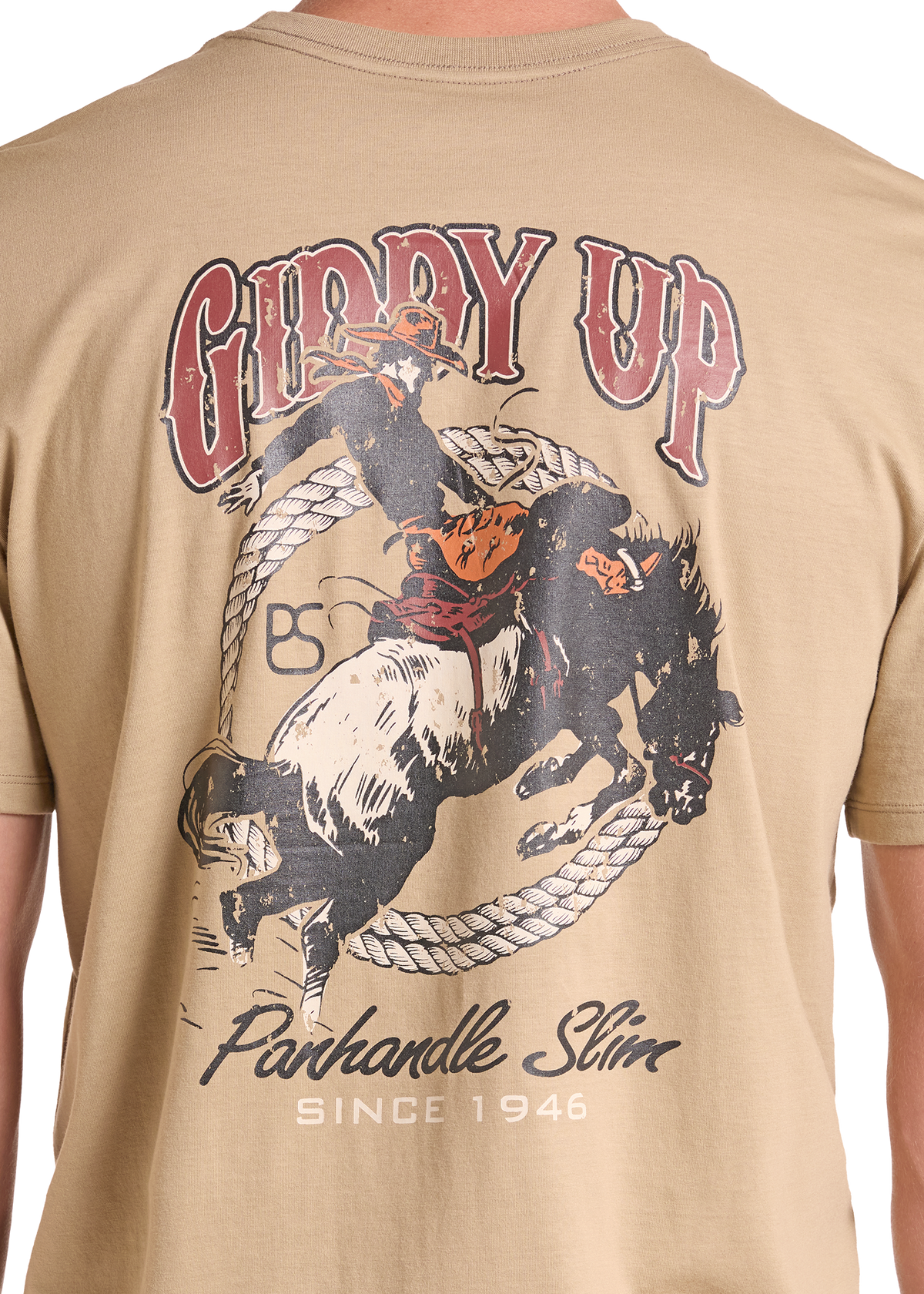 A close-up of a tan t-shirt showing the back graphic. The graphic features a cowboy riding a bucking bull inside a lasso, with the text 'GIDDY UP'.