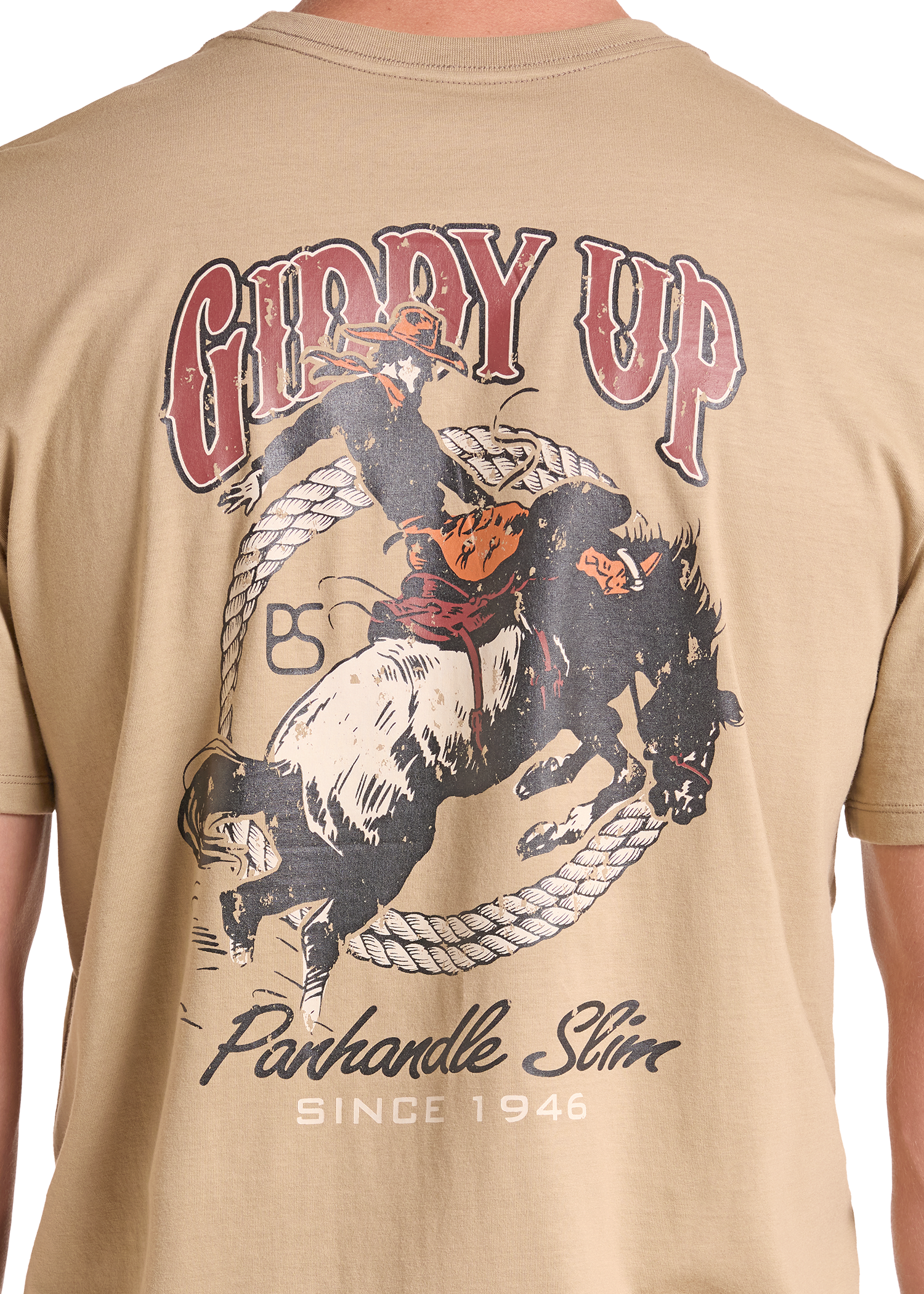 A close-up of a tan t-shirt showing the back graphic. The graphic features a cowboy riding a bucking bull inside a lasso, with the text 'GIDDY UP'.