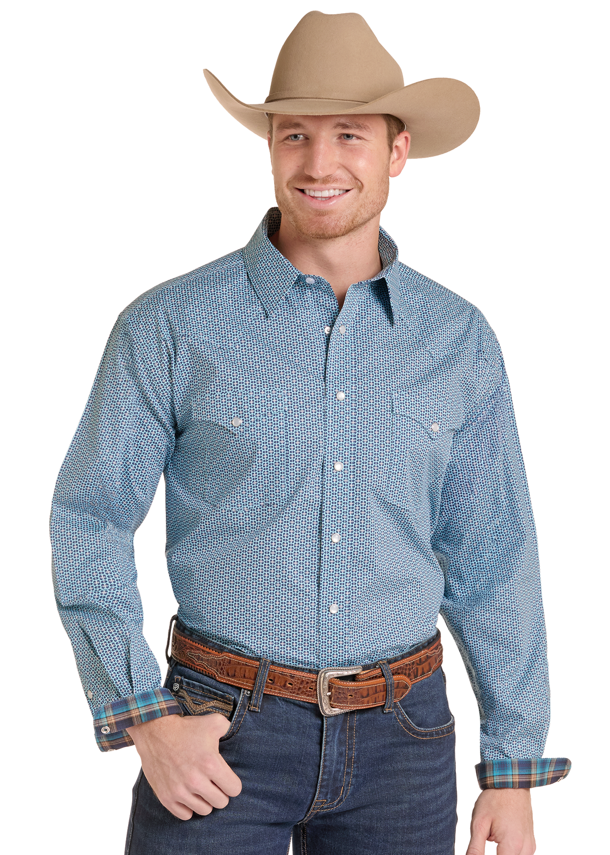 A smiling man wearing a light blue patterned western long-sleeve button-up shirt, dark blue jeans, a brown leather belt, and a tan cowboy hat.