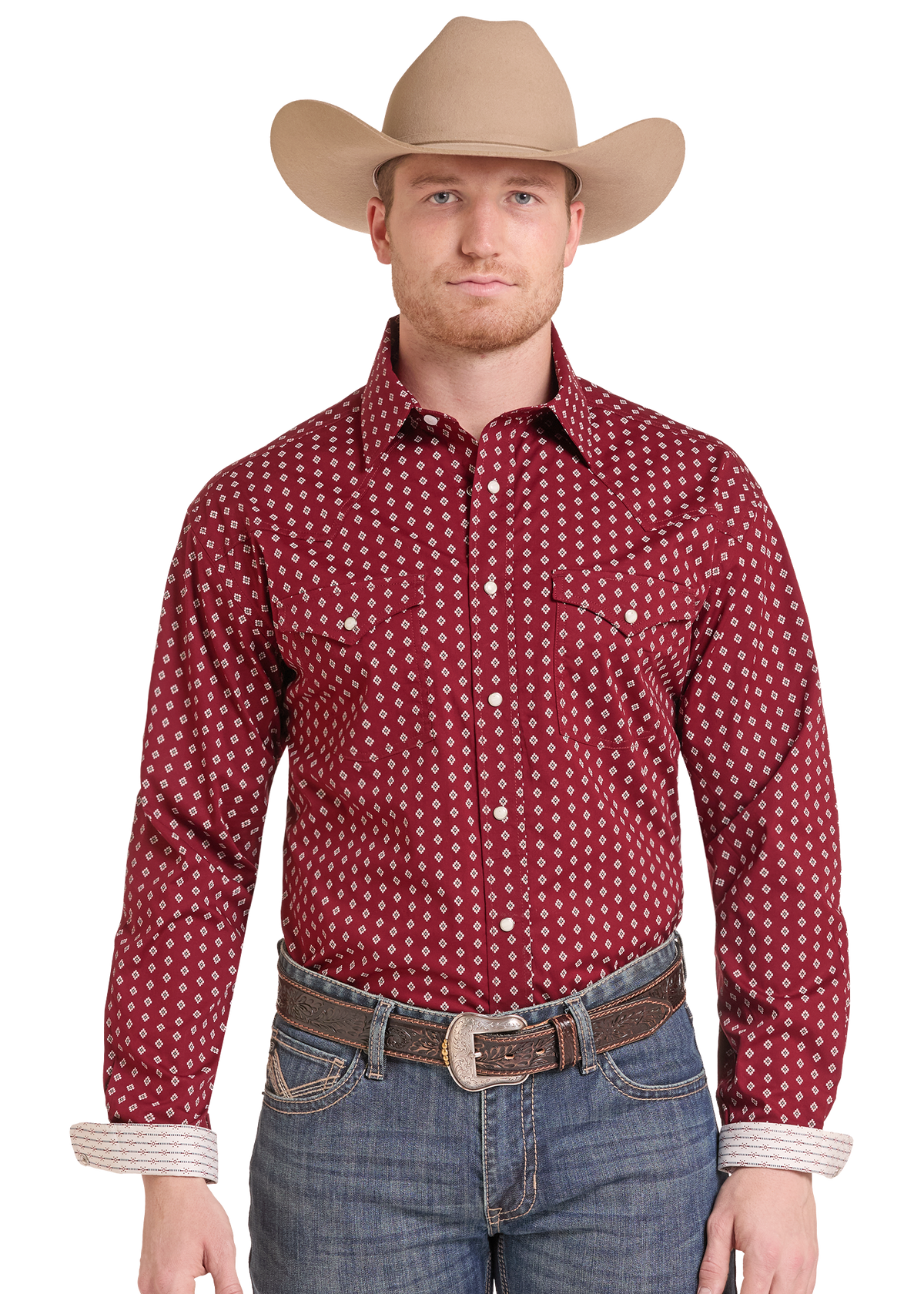 A man wearing a red western long-sleeve button-up shirt with a white geometric pattern, paired with a tan cowboy hat, brown belt, and blue jeans.