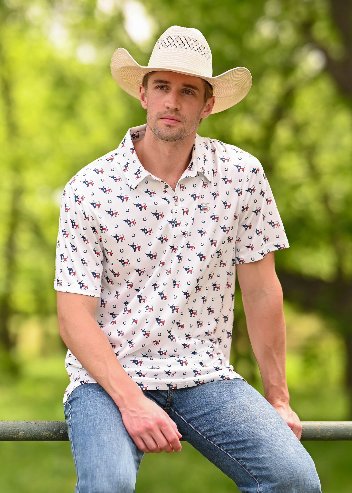 Man wearing a polo with horse shoes, longhorns and Texas flags on it while sitting on a rusty fence. 