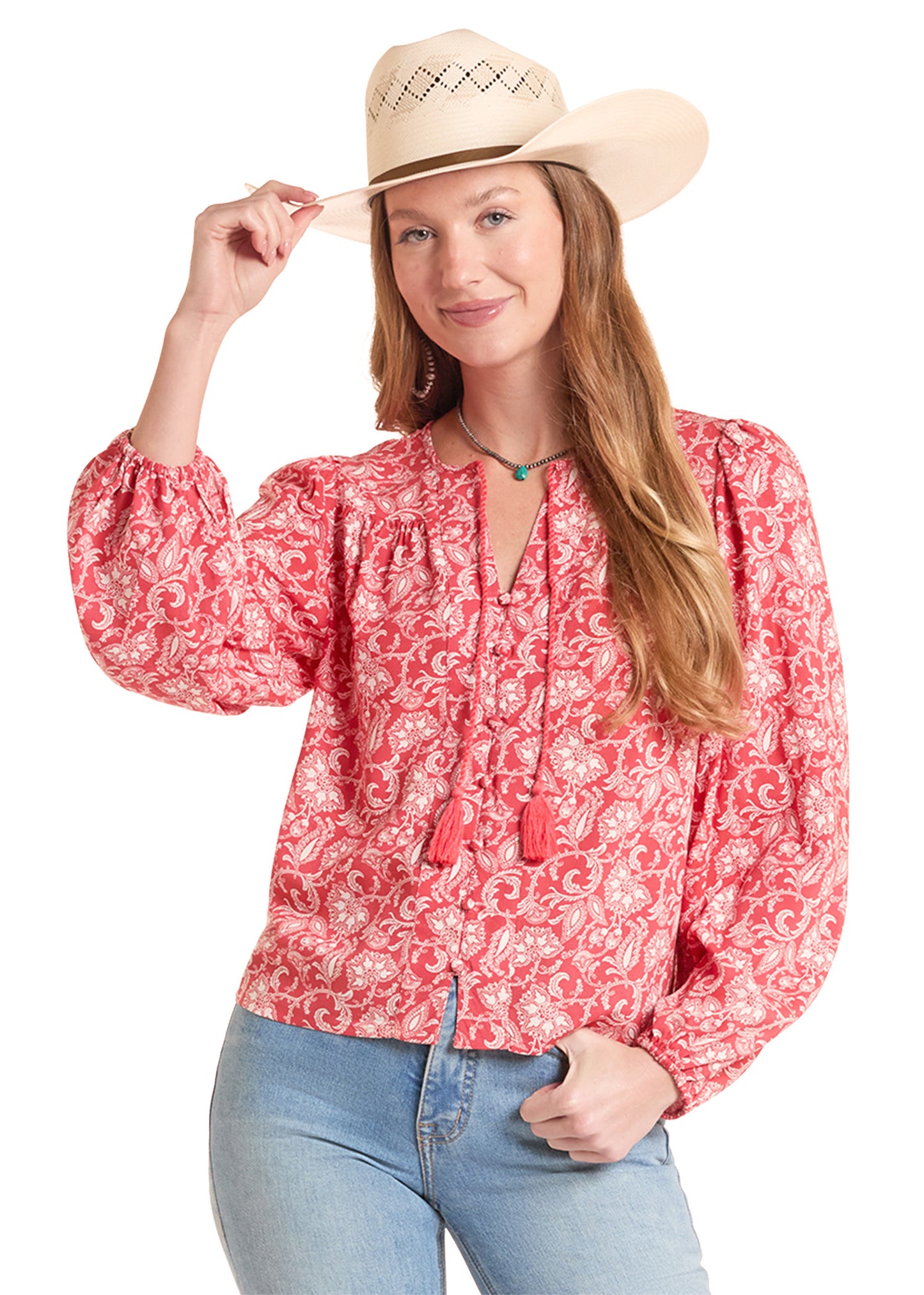 Woman wearing a red patterned blouse, blue jeans, and a beige hat on a white background