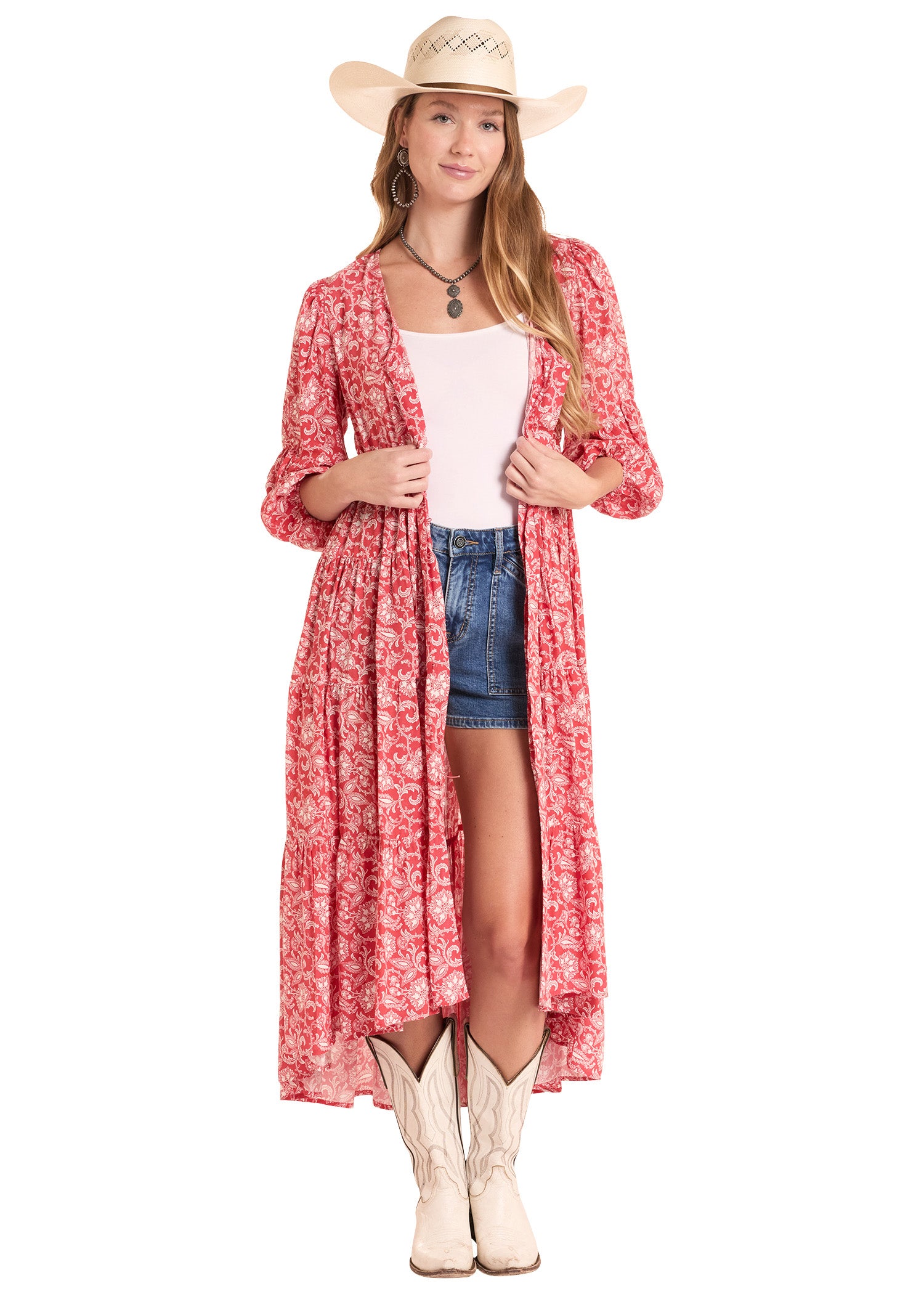 Woman wearing a red floral dress over a white top and denim shorts, with a cowboy hat and boots on a white background.