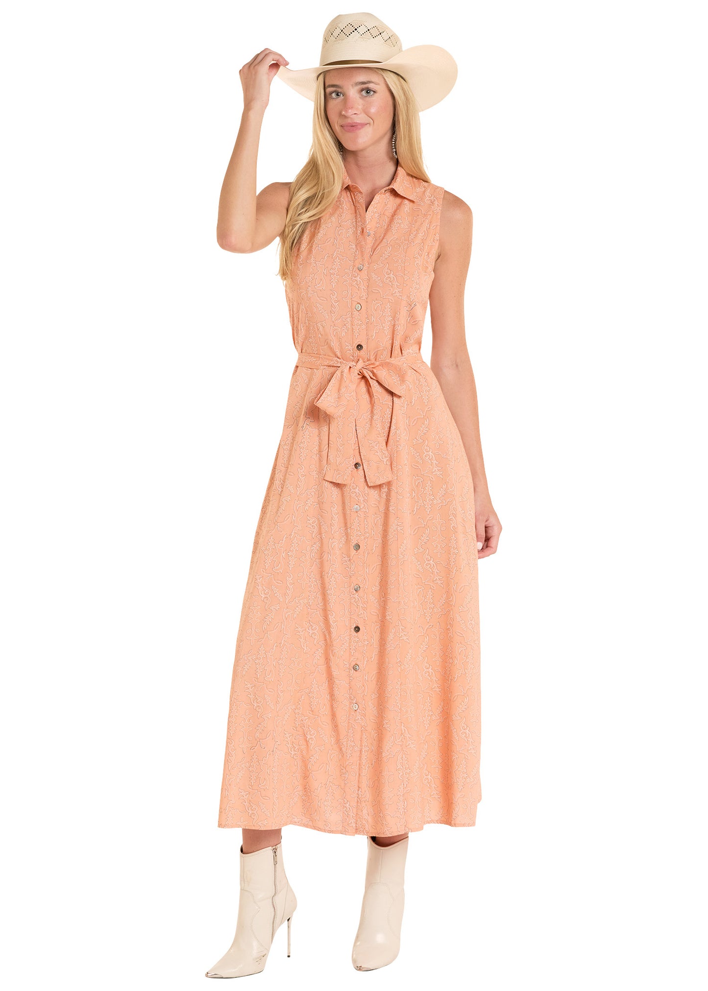 Woman wearing a peach sleeveless dress with a belt, white boots, and a straw hat on a white background
