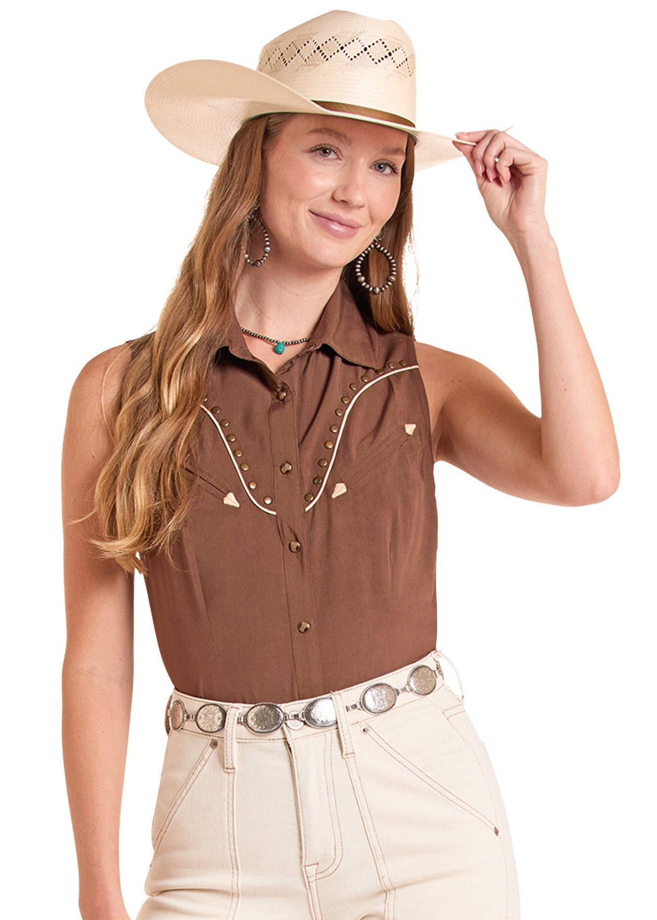 Woman wearing a brown sleeveless shirt with white embroidery, beige pants, and a beige cowboy hat on a white background.